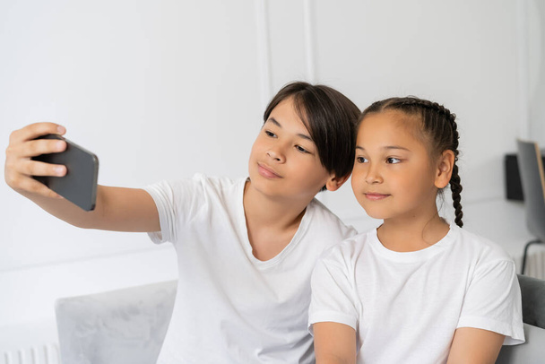 Preteen asian boy taking selfie on cellphone with sister at home  - Фото, зображення