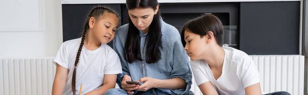 Femme utilisant un smartphone près des enfants asiatiques dans le salon, bannière  - Photo, image