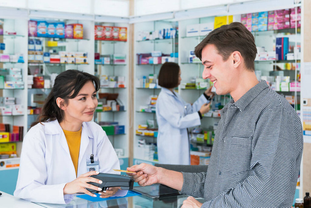 Payment by credit card with payment terminal in qualified drugstore. Modern financial payment of electric money. Caucasian customer purchase medication in pharmacy with prescription from pharmacist. - Photo, Image