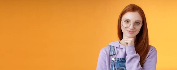 Sebevědomý šťastný uvolněný evropský ryšavý zručný mladá žena podnikatelka brýle vytvořit startup usmívat potěšený vzhled potěšený výsledek dotek bradu přemýšlivý inteligentní, oranžové pozadí. - Fotografie, Obrázek