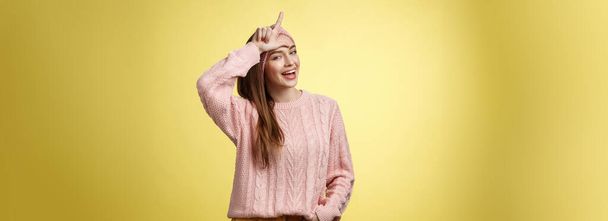 Attractive triumphing arrogant and confident cute glamourous woman in knitted sweater, headband showing l letter on forehead, loser sign and laughing over lost team, mocking having fun. Copy space - Photo, Image