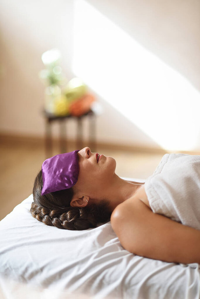 Vrouw liggend voor massage met zaadzak op ogen in verticaal vlak - Foto, afbeelding