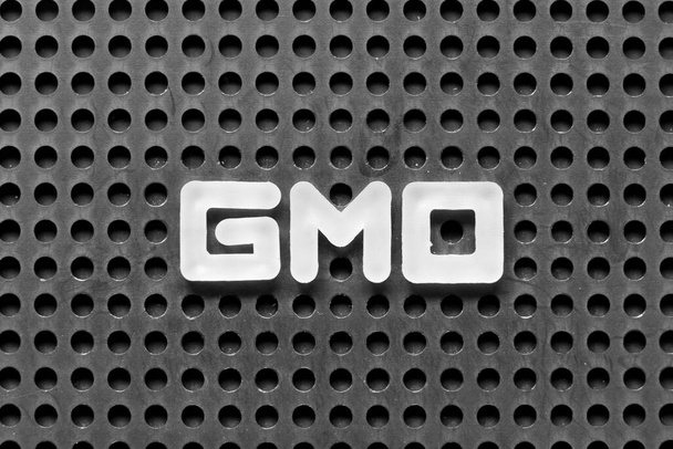 Biała litera alfabetu w słowie GMO (skrót od organizmów zmodyfikowanych genetycznie) na czarnym tle pegboard - Zdjęcie, obraz