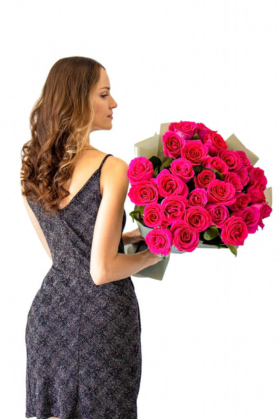 Красива молода жінка з букетом рожевих троянд на ізольованому білому тлі. Дівчина в елегантній чорній сукні з її спиною до камери
. - Фото, зображення