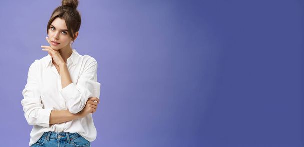 Porträt einer zarten und femininen stilvollen Frau in weißer Bluse, die sinnlich posiert und ihr kokett berührendes Kinn waghalsig in die Kamera starrt und vor lila Hintergrund mit selbstsicherem Ausdruck posiert. Kopie - Foto, Bild