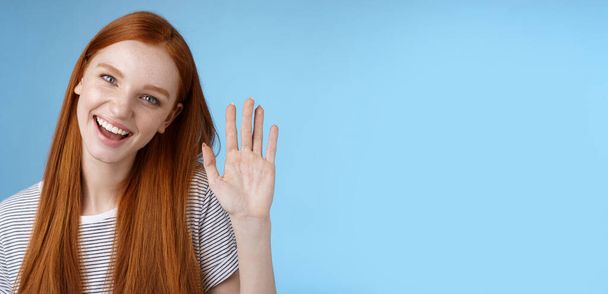 Attractive confident redhead sassy girl pure clean skin blue eyes tilting head cheerfully waving hand hello hi gesture greeting you look camera friendly welcoming friend, standing studio background. - Photo, Image