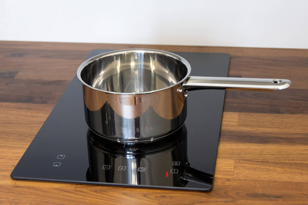 Saucepan lepel op een inductie kookplaat ingebouwd in een houten keukenblad - Foto, afbeelding