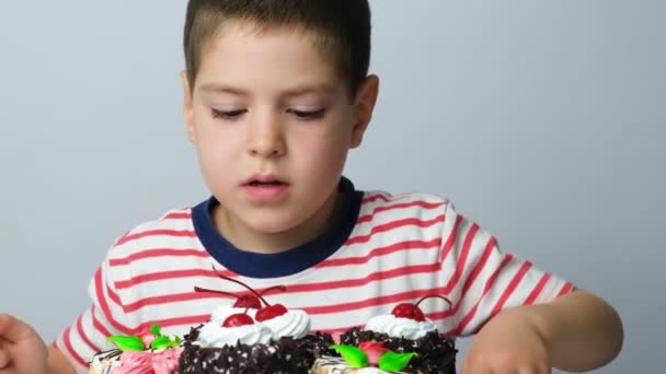 Un niño preescolar con una camiseta a rayas se está preparando para comer una gran tarta deliciosa - Imágenes, Vídeo
