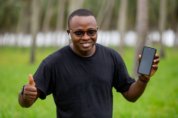 A fiatal afrikai mezőgazdasági mérnök egy üres képernyős okostelefont használ mezőgazdasági területen. a növények növekedésének figyelemmel kísérésére. - Fotó, kép