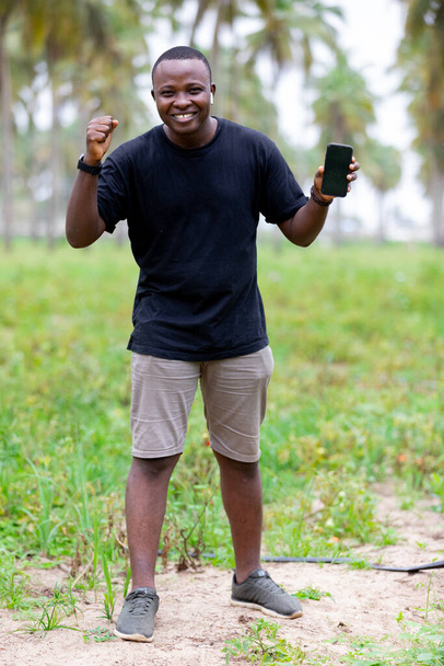 Afrika 'daki köyün neşeli, gülümseyen siyahi Afrikalı genci boş ekranı işaret ediyor.. - Fotoğraf, Görsel