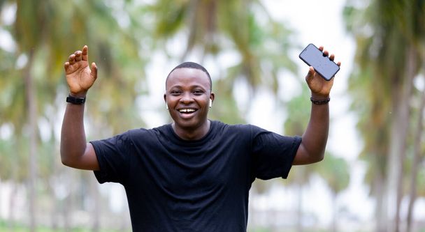 Vidám mosolygós fekete afrikai fiatalember a faluban Afrikában ujjal mutogatva az üres képernyőre okostelefon. - Fotó, kép