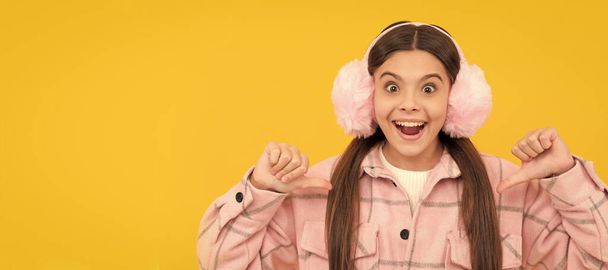 Happy kid in warm winter fur ear warmers smile pointing thumb fingers at herself, fashion. Child face, horizontal poster, teenager girl isolated portrait, banner with copy space - Foto, afbeelding