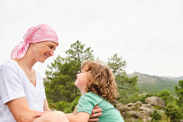 Мать с раком и сын, смотрящие друг на друга расслабленно на горе. На ней розовый платок.. - Фото, изображение
