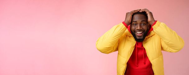 Waist-up verrast gelukkig geluk jonge Afrikaans-Amerikaanse bebaarde man in geel jasje hand in hand hoofd glimlachend onder de indruk blij ontvangen geweldig aanzoek droom uitkomen, roze achtergrond. - Foto, afbeelding
