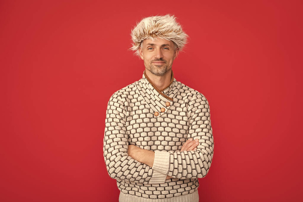 mature guy portrait. positive man in earflap hat. grizzled guy in sweater on red background. hoary man wear warm hat. male winter fashion. mens beauty. - Fotoğraf, Görsel