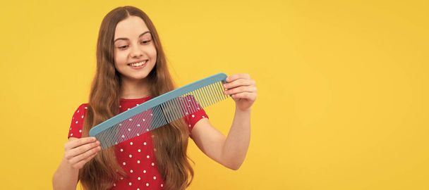 happy kid brushing long hair with comb on yellow background, haircare. Kid girl hair care, horizontal poster. Banner header with copy space - Photo, image