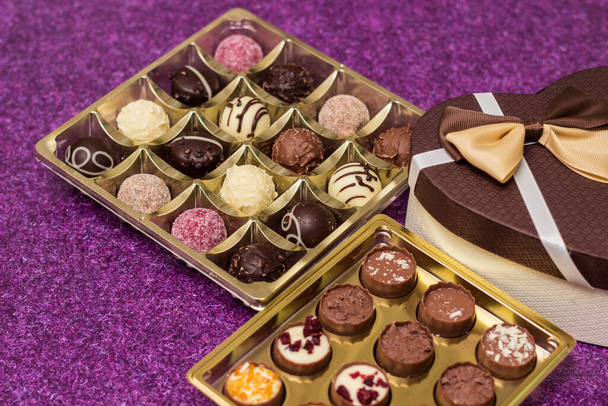 Doos met heerlijke chocolade snoepjes en hartvorm cadeau, op paarse tafel - Foto, afbeelding