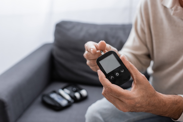 gedeeltelijk zicht op man van middelbare leeftijd met diabetes met glucosemeter en teststrip - Foto, afbeelding