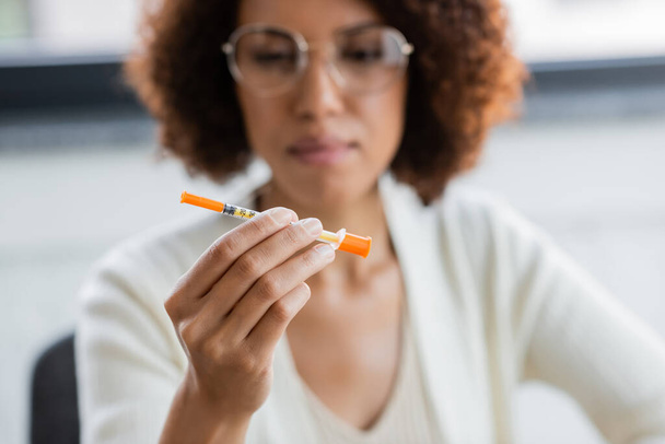 Blurred african american businesswoman with diabetes holding syringe in office  - Photo, Image