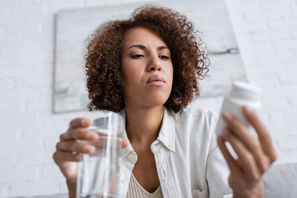 Low angle view van Afrikaanse Amerikaanse vrouw met diabetes houden wazig pillen en water thuis  - Foto, afbeelding