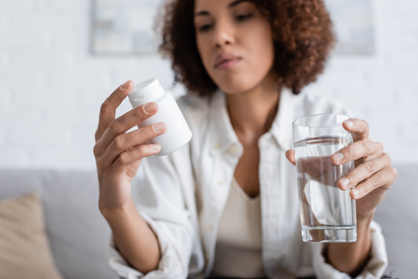 Femme afro-américaine floue avec diabète tenant des pilules et de l'eau à la maison  - Photo, image