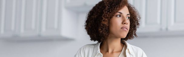 Jeune femme afro-américaine regardant loin dans la cuisine floue, bannière  - Photo, image