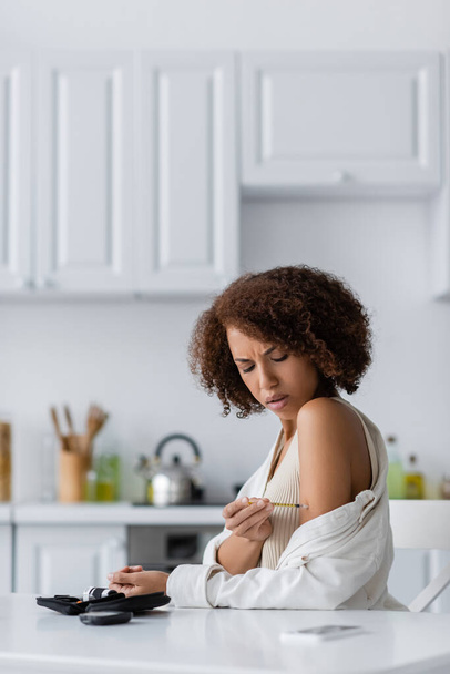 Młoda Afroamerykanka wykonuje wstrzyknięcie insuliny w pobliżu telefonu komórkowego i zestawu cukrzycowego w kuchni  - Zdjęcie, obraz