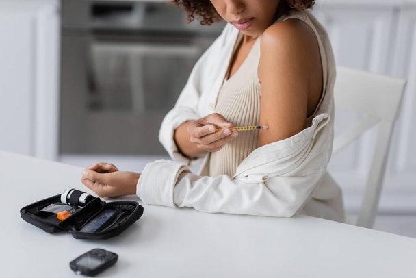 Vue recadrée du kit diabète près d'une femme afro-américaine faisant une injection d'insuline à la maison  - Photo, image