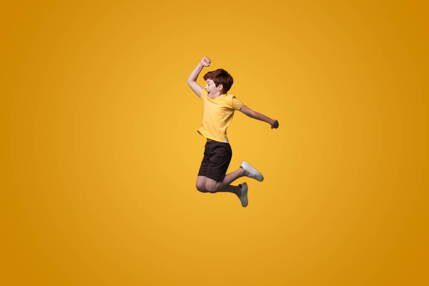 Πλήρης φωτογραφία του μικρού αγοριού άλμα απομονωμένο παστέλ κίτρινο χρώμα φόντο. Ευτυχισμένοι άνθρωποι θετικά συναισθήματα. Σχέση δραστηριότητας. Χαμογελάστε συναισθήματα. - Φωτογραφία, εικόνα