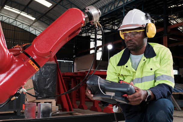An African American production engineer test and control robotic arm in mechanical manufacturing factory, intelligent automatic machines in industrial business, and futuristic technology innovation. - Photo, Image