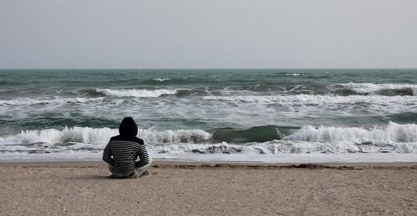 Homem sentado em uma praia e olha para o mar
 - Foto, Imagem