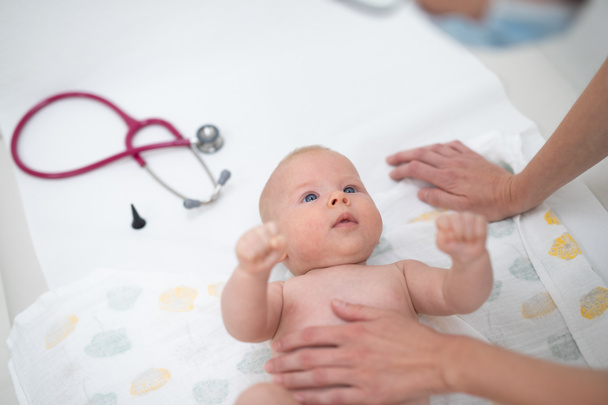 Bebé acostado boca arriba mientras su médico lo examina durante un chequeo médico estándar
. - Foto, Imagen