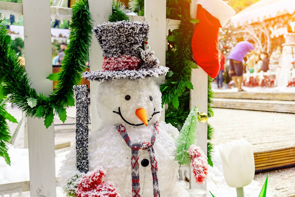 Декоративное украшение искусственного снеговика у входа в небольшой жилой микрорайон. Снеговик стоит перед общественным парком на рождественские праздники. Концепция Рождества и Нового года. - Фото, изображение
