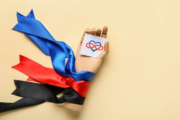 Wooden hand, paper with symbol of polyamory and ribbons on color background - Photo, Image