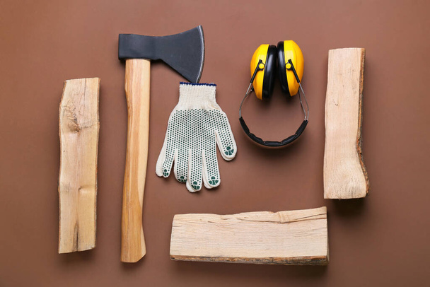Ax with firewood, gloves and hearing protectors on brown background - Photo, Image