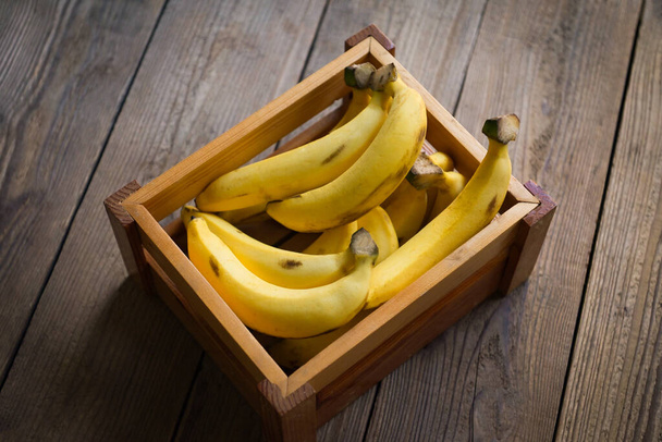 Bananenstrauß - Banane auf Holzkistenhintergrund, reife Bananenfrüchte auf dem Boden - Draufsicht - Foto, Bild