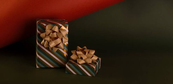 Boxing Day concept with gift boxes in gold and green colors decorated with sparkling bow against deep green and brick color paper background. - Φωτογραφία, εικόνα