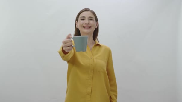 Character portrait of a young woman drinking a cup of coffee, black or green tea. Young healthy woman smelling, drinking and pointing to camera a cup of coffee or tea isolated on white background. - Footage, Video