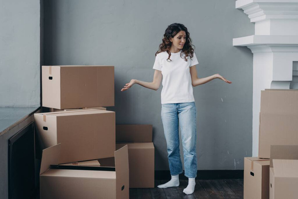Puzzled female tenant shrugging looking around, suffers stress with packing things and leaving rented apartment. Tired girl standing with cardboard boxes in vacated house. Hard relocation day. - Photo, Image