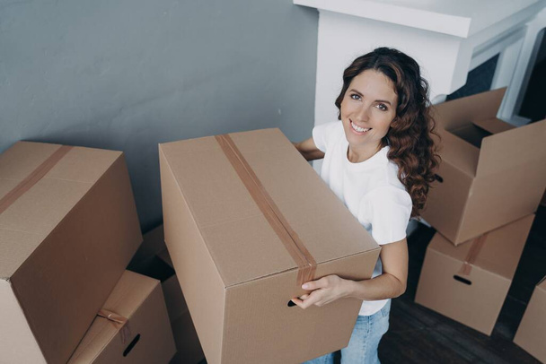Happy hispanic woman volunteer holding donation box with things. Smiling female preparing parcels, packing items into carton boxes to donate to charity during relocation. Charitable activity concept. - Photo, Image