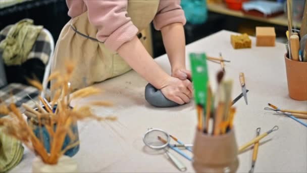 De meester van het beeldhouwen aardewerk werken in een atelier. Ze kneedt een stuk klei met haar handen. Gereedschap op tafel. Langzame beweging - Video
