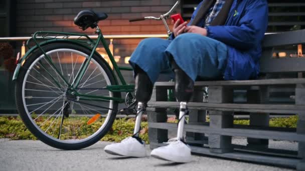 Vista de um homem com pernas protéticas. Levantar-se do banco e sair com sua bicicleta - Filmagem, Vídeo