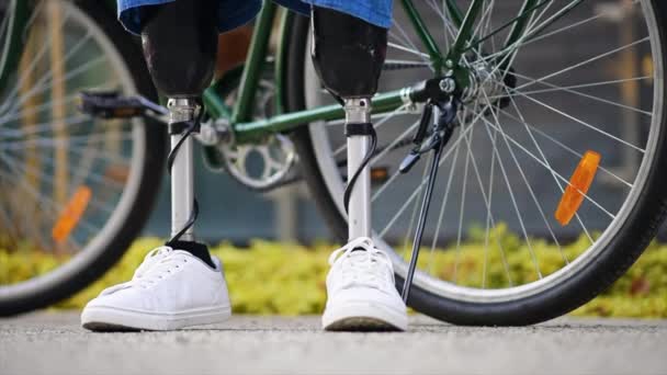 Slow motion view of a man with prosthetic legs. Standing next to his bicycle - Footage, Video