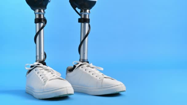 Vue d'un homme avec des jambes prothétiques et des baskets blanches debout sur un fond bleu - Séquence, vidéo