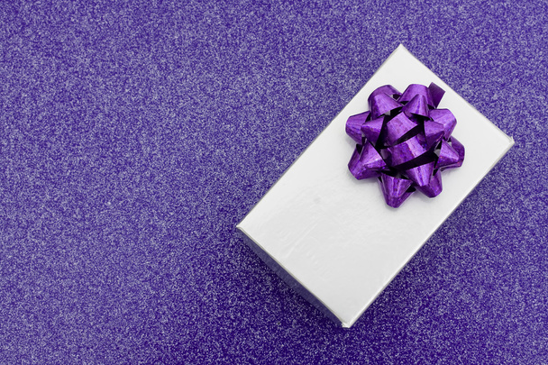 ein silbernes Geschenk mit Schleife auf violettem Hintergrund - Foto, Bild
