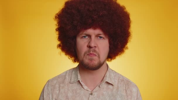 Offended bearded man with afro hairstyle coiffure having misunderstanding, showing tongue, frustrated after quarrel, ignores and does not want to communicate, talk. Hipster guy on yellow background - Footage, Video