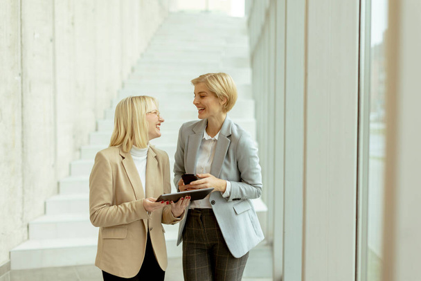 Due donne d'affari che camminano con laptop e telefono cellulare nel corridoio dell'ufficio - Foto, immagini