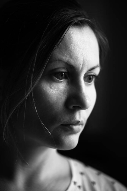 Pencereden ışık süzülen bir kadının tek renkli portresi, genç yorgun bir kadının portresi.. - Fotoğraf, Görsel