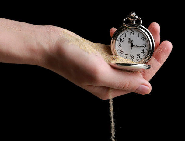 Srebrny kieszonkowy zegar w ręce i piasek, płynącej od na czarnym tle - Zdjęcie, obraz