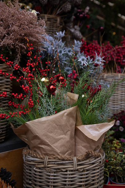 Festive Christmas bouquets of twigs of thuja, coniferous pine tree, ilex verticillata winterberries, decorated with Christmas balls in the basket at the greek garden shop counter in December.Vertical. - Photo, Image